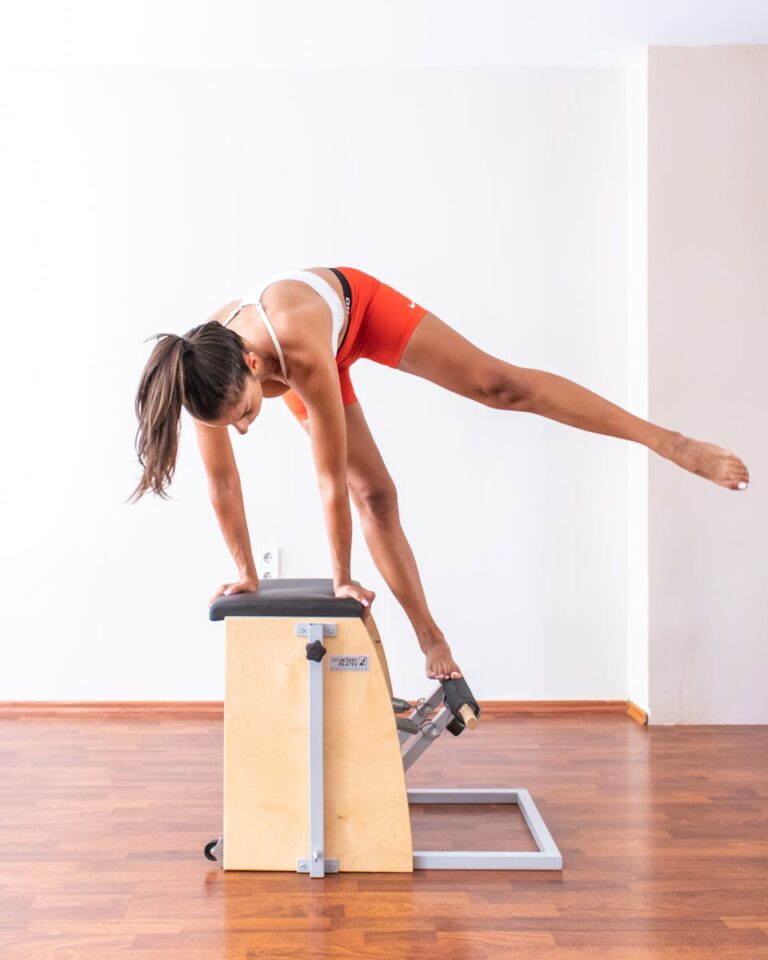 An athletic woman practicing Pilates on a Wunda Chair in a bright indoor setting for fitness training.