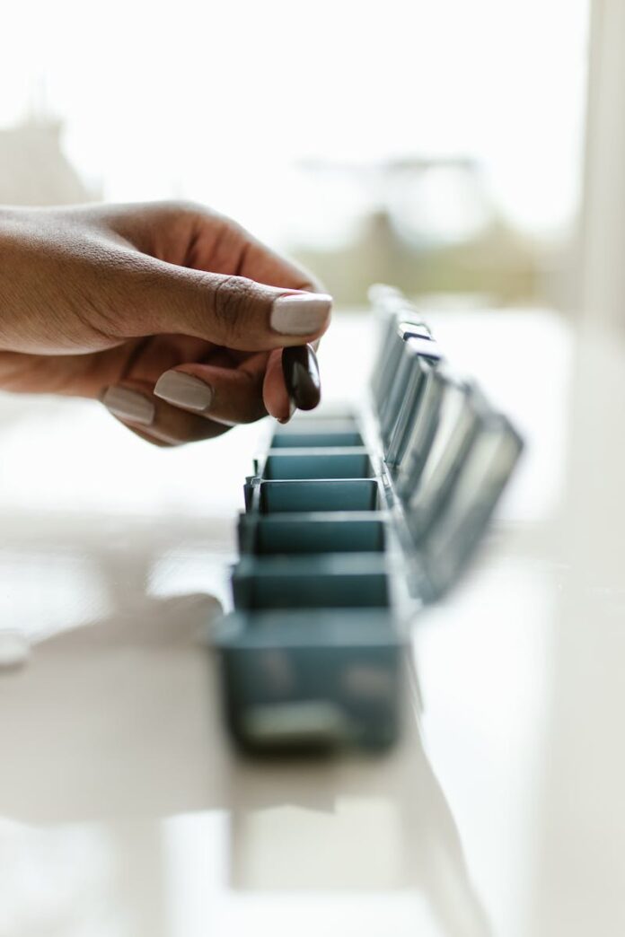 Close-up of a hand holding a pill above a weekly pill organizer, emphasizing medication routine.