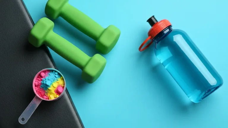 Porcja proszku pre-workout w miarce obok hantli i butelki wody na siłowni